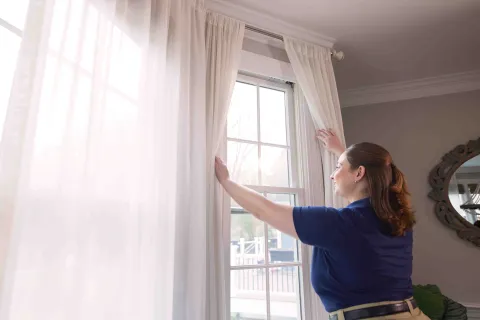 a person in a blue shirt opening curtains